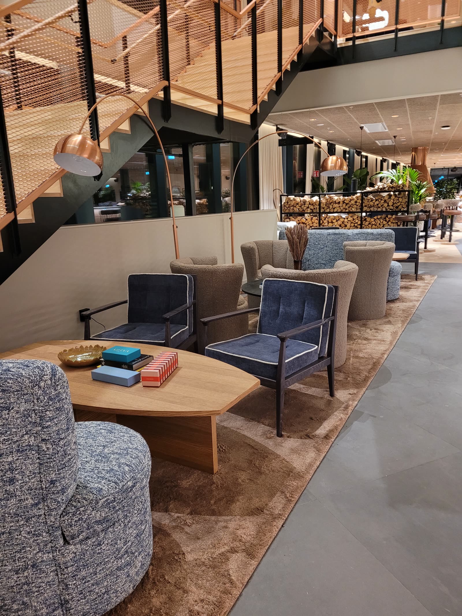 Hotellobby med blå velurfåtöljer och bouclésoffor under kopparlampor